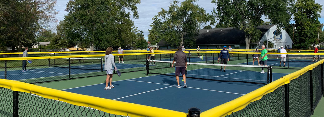 a group of community members playing on a blue pickleball court, surrounded by trees
